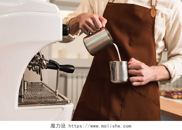 咖啡师正在往咖啡杯中倒入牛奶棕色围裙咖啡师在钢杯中倒入牛奶的裁剪视图